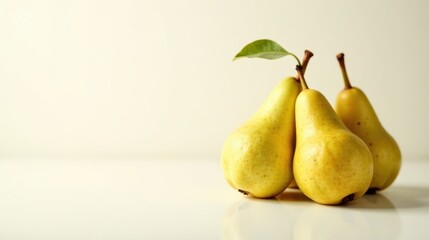 Three Ripe Yellow Pears with a Single Green Leaf Resting on a Pristine White Surface