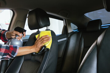 A professional car cleaner meticulously washing a shiny vehicle using a pressure hose and foam. The man focuses on the car's exterior, ensuring a spotless, polished finish at an auto detailing station