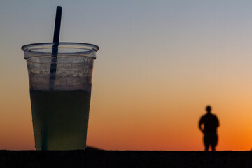 Refreshing cocktail in focus at golden hour, with a beach setting and warm sunset tones in the background.