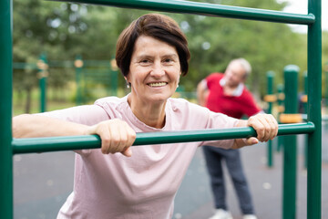 Obraz premium Mature woman doing push-ups from the crossbar on outdoor sports ground