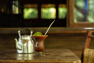 bebida quente típica do sul do Brazil, chimarrão e chaleira em cima da mesa de madeira em galpão rústico
