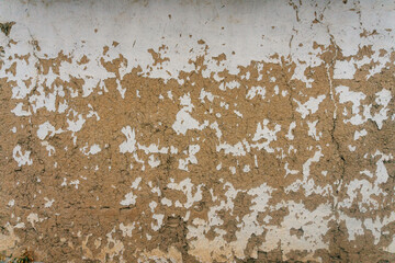 wall of house built with hay and clay. paint peeling off from wall. texture of clay and light paint
