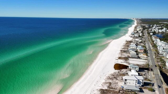A panoramic aerial shot highlighting the stunning contrast of white sand, emerald green shallows, and deep blue waters along the coastline of Route 30A at Panama City Beach, Florida.
