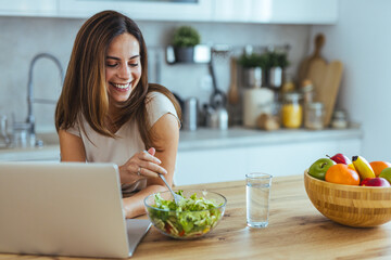 Woman Enjoying Healthy Salad While Working on Laptop in Modern Kitchen