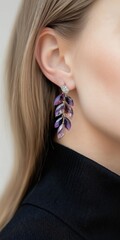 A woman wearing a purple earring with a leaf design. The earring is made of crystals and is hanging down from her ear