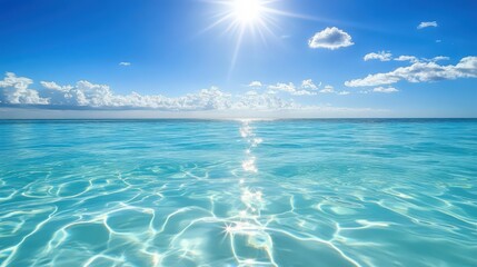 Sunlit turquoise ocean reflecting sunlight with puffy clouds in bright blue sky