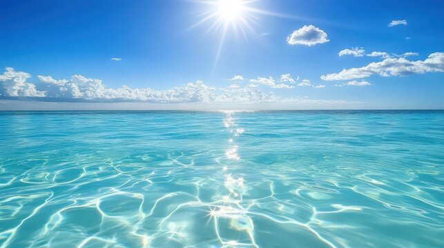 Sunlit turquoise ocean reflecting sunlight with puffy clouds in bright blue sky