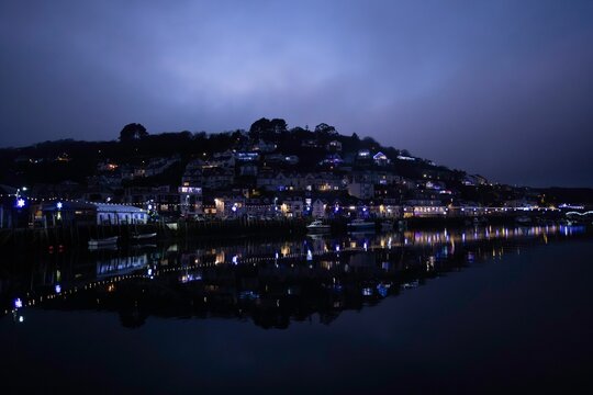 Scenic night view of a coastal town with illuminated buildings reflecting on calm water