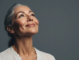 A woman with gray hair, smiling gently and looking into the distance. She is wearing a white top, possibly in meditation or thoughtful contemplation.