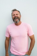 A man in a pink shirt is smiling and laughing. He is standing in front of a white wall