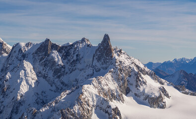 Naklejka premium Breathtaking panoramic view of the snow-covered Alps from Aiguille du Midi, Chamonix. Majestic peaks, deep valleys, and vast glaciers under a clear blue sky create an unforgettable alpine scenery.