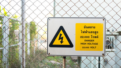 Electrical high voltage caution sign plate (In Thai and English text)  that installed on wire fence of power supply station. Sign and symbol for industrial, close-up with selective focus.