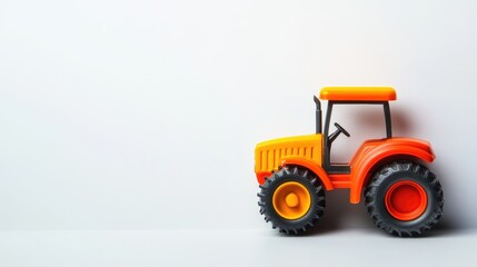 Naklejka premium Vibrant orange and yellow plastic toy tractor positioned on a clean white surface with ample negative space for text or graphics.