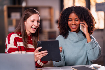 Two businesswomen working overtime, chatting in the office, working with laptops, documents, graphs, financial analysis with lights in the office