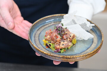 Man presenting a rustic plate of tuna tartare with mango and avocado, held in his palm. A fresh and elegant dish combining vibrant colors, fine vingredients, and modern culinary style in a natural,