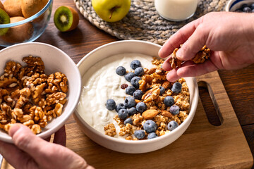 Greek yogurt with granola, fresh blueberries, and almonds on a wooden table. A quick and healthy breakfast concept
