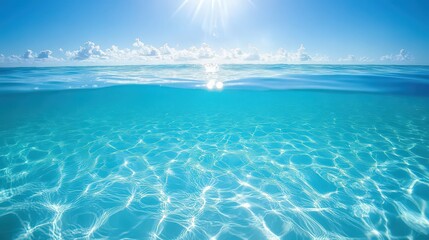 Clear turquoise ocean water meets bright blue sky with fluffy white clouds and sun