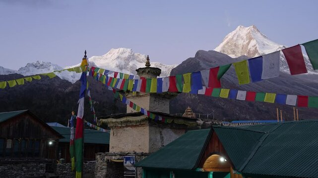 Manaslu, Nepal: Panoramic view of the sunrise over the Manaslu peak and the Shyala village Tibetan Buddhist stupa that is decorated with prayer flags in the Himalaya in Nepal. 