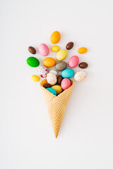 Ice cream cone with colorful chocolate Easter eggs on white background. Minimal creative Easter concept. Trendy festive spring holiday idea. Easter aesthetic. Flat lay, top of view.