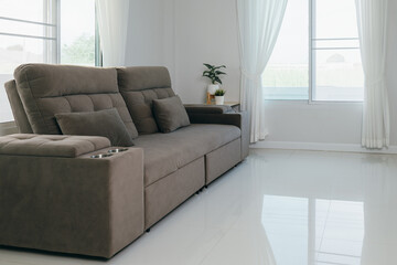 A modern gray sofa with two pillows and built-in drink holders, placed in a bright room with white...