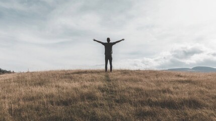 Man standing on hilltop, arms outstretched, enjoying nature.
