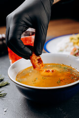 Black-gloved hand dipping crispy bread in a bowl of hearty soup for a delicious meal moment