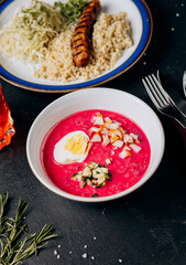 Colorful business lunch with grilled sausage, couscous, cabbage salad, and beet soup with boiled egg