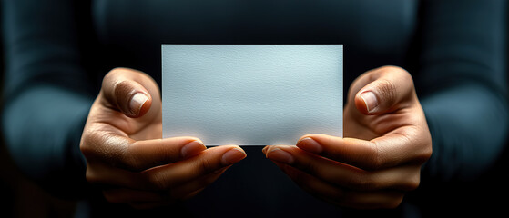 Obraz premium Person holding a blank card with both hands in a dimly lit environment focusing on the blank surface. Generative AI
