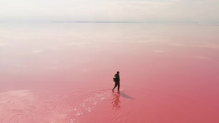 A lone traveler with a backpack walking gracefully across a vibrant pink salt lake, surrounded by stillness. Captures the essence of exploration, adventure, and natural beauty. - Powered by Adobe