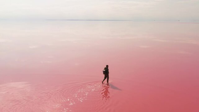 A lone traveler with a backpack walking gracefully across a vibrant pink salt lake, surrounded by stillness. Captures the essence of exploration, adventure, and natural beauty. 