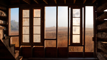 A composite landscape of a field with fog in the early morning as seen through the broken walls of an old cabin