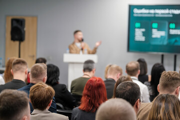 Obraz premium Speaker delivers presentation to attentive audience at business event. Large screen displays data on stage. Professional setting promotes learning and networking among attendees.