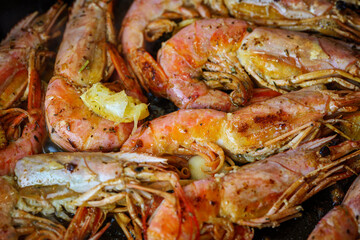 Grilled langoustine shrimps, prawns in a frying pan. Cooking langoustine on frying pan with butter, lemon and garlic. Langostino Austral or scampi on a black frying pan.