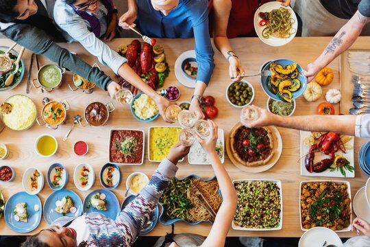 A diverse group enjoying a meal together, sharing food and drinks. Top view of a table with various dishes, showing a sense of community and celebration. Diverse people celebrating and toasting.