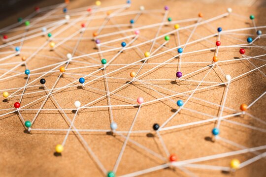 Colorful pins connected by strings on a corkboard background. Network of pins and strings creating a web. Pins and strings forming a complex pattern on corkboard. Business nework background.