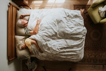 Elderly couple sleeping in bed, covered with a white blanket. Peaceful, cozy bedroom setting with...