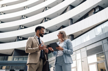 Business people having conversation holding digital tablet outside office building