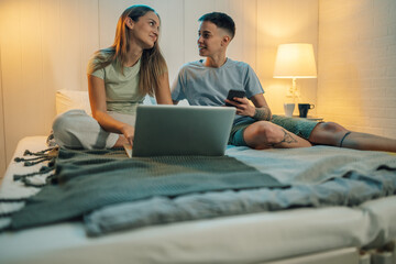 Lesbian couple using laptop and smartphone in bed at home
