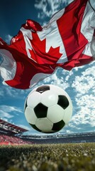 Fototapeta premium Classic black-and-white football in focus in mid-air with Canadian flag waving above, in a stadium under a vibrant blue sky.