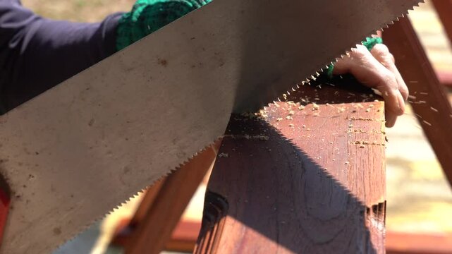 Carpenter saws wood with a saw.