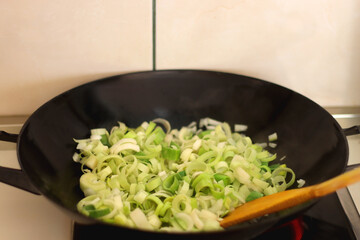 Sauteing chopped leek slices in a wok. Selective focus.