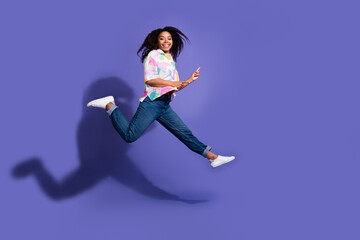 Young woman in casual attire joyfully jumping against a vibrant purple background, exuding energy and happiness.