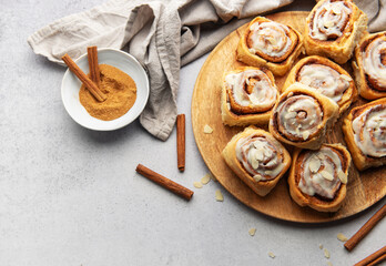 Freshly baked cinnamon rolls with icing and almond flakes on wooden tray