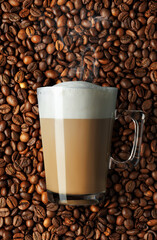 cappuccino in glass cup and coffee beans as background