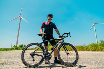 Fototapeta premium Cyclist poses confidently with bicycle near wind turbines in sunny landscape