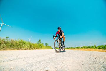 Fototapeta premium Cyclist navigating a gravel road surrounded by wind turbines on a sunny day