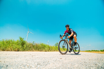 Obraz premium Cyclist riding on a gravel road with wind turbines in the background under a clear blue sky