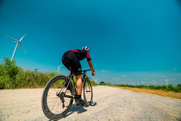 Obraz premium Cyclist enjoying a sunny ride on a gravel road with wind turbines in the background