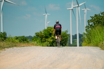 Obraz premium Cyclist navigating a gravel road surrounded by wind turbines under a blue sky on a sunny day