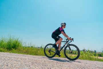 Fototapeta premium Cyclist riding on a gravel path under a clear blue sky in a sunny outdoor setting